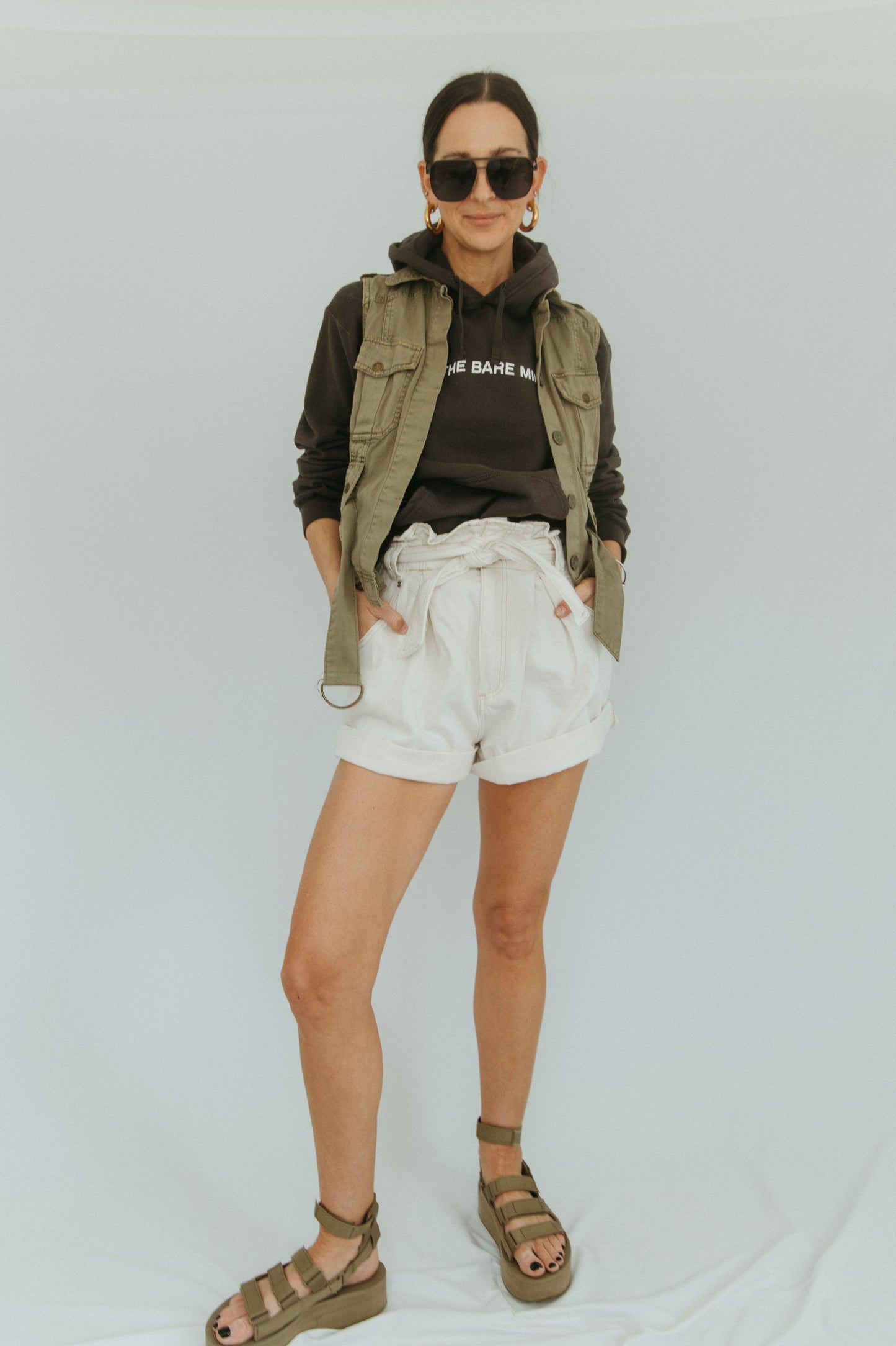 Steel grey hooded sweatshirt with white writing that says 'Doing The Bare Minimum' across the chest; white logo on the sleeve above the wrist